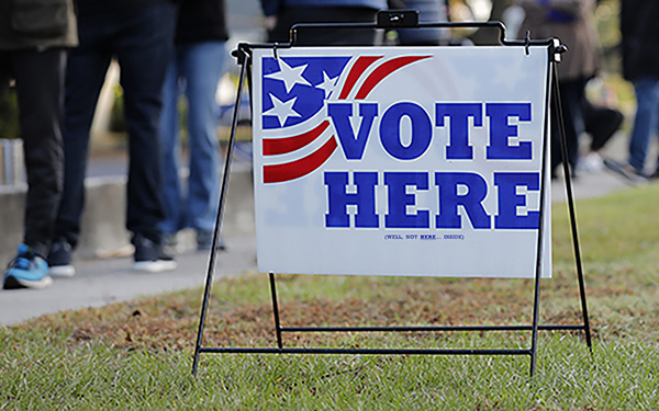 Graphic showing a paper voting slip sticking out of a ballot box. Background shows the American flag