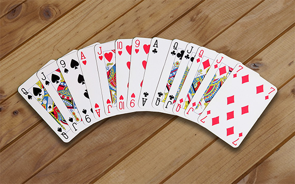 A photograph of thirteen playing cards laying on a wooden background